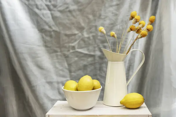 乾いた花と熟したレモンが付いたホワイトボウルとエナメルシートの金属ジャグでまだ生きている — ストック写真