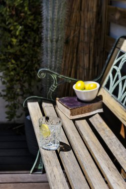 Terastaki ahşap bir bankta limon dilimli berrak bir cam bardak.