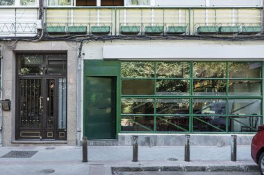 Sokak seviyesindeki cam ve demir kaplamalı bir ticari binanın ön görüntüsü yeşile boyanmış.