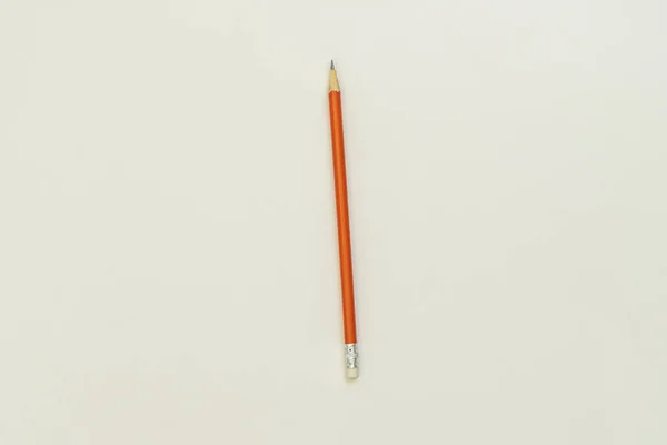 滑らかな白い表面の片端に小さな消しゴムが付いている鋭いオレンジ色の鉛筆 — ストック写真