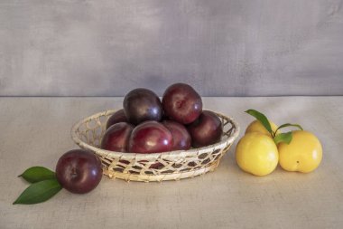 Birkaç olgun sarı erik ve yeşil yaprakları açık ahşap bir masada duran kırmızı eriklerle dolu bir sepet.