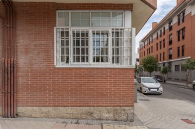 Şehir merkezindeki bir binanın asma katında metal parmaklıklı beyaz pencereler.