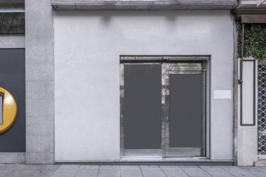 Sokak seviyesinde diğer binaların yanında cilalı çelik kapılı bir ticari tesisin cephesi.