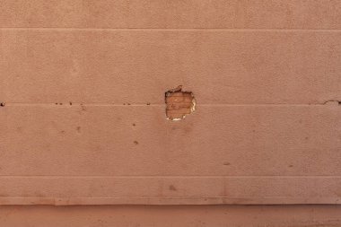 Tuğlaları ve kahverengi boyayı ortaya çıkaran delikli bir bina duvarı.
