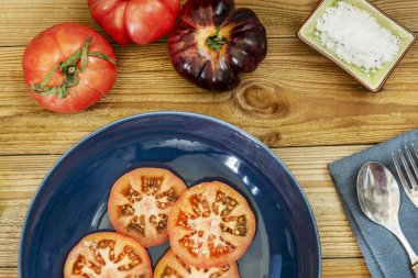 Tahtada domates dilimleri olan mavi bir tabak. 