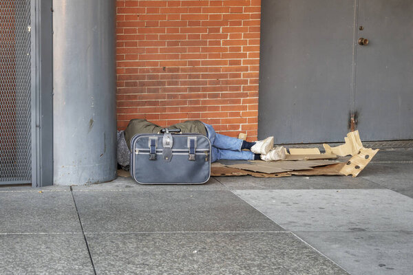 Бездомный спит на картонке на углу улицы.