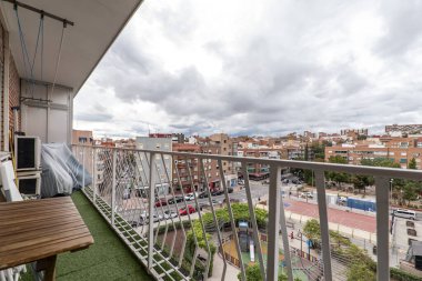 Beyaz korkuluklu, tavanında çamaşır ipi olan yapay çim zeminli bir teras.