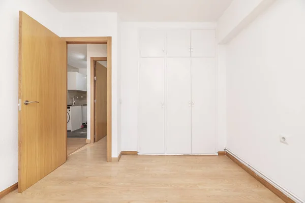 An empty room with a built-in wardrobe with white doors, freshly painted smooth walls