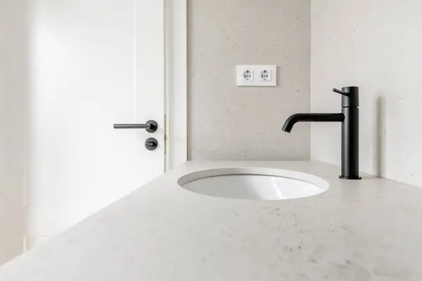 Image of the bathroom with cream tiles, matching countertop, matching black faucets