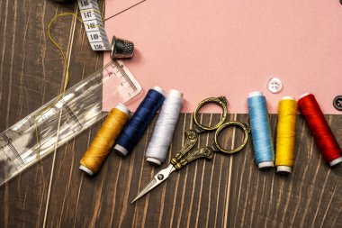 Plastik cetvel, mezura, çeşitli iplikler, kahverengi ahşap masadaki altın antika makaslar...