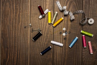 Sarı iplikli bir iğne, biraz çengelli iğne, bir mezura ve ahşap arka plan.