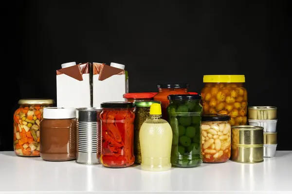 Glass jars with tomato sauce, cans of canned fish, a large jar of olives, strips of piquillo peppers, vegetables and some drink cartons