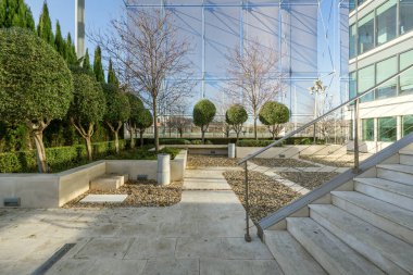 Beyaz taşlı, ağaçlı, çitli ve gölgeli bir ofis binasının terası.