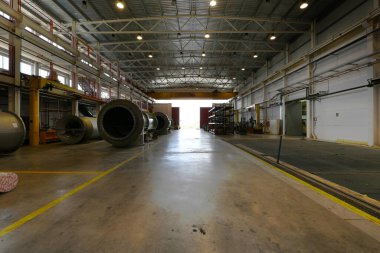 Çatı raylarında ağır vinçleri, büyük mekanik parçaları ve beton zemini olan bir fabrikanın deposu.