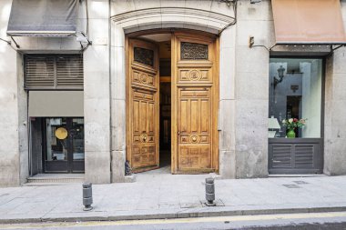 Sokak seviyesindeki birkaç ticari tesisin içinde ahşap panelli kapısı olan eski bir konut binasının ön cephesi.