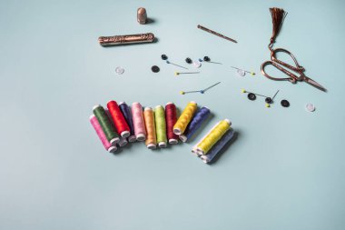 Pürüzsüz mavi bir yüzey üzerinde çok renkli ipliklerin yeni makaraları iğne, iğne, iğne, siyah ve beyaz düğmeler ve klasik makaslarla birlikte.