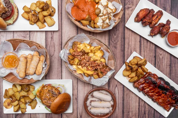 Set of international fast food dishes, barbecue ribs, hamburgers, patatas bravas, Venezuelan teques, chicken wings with sauce and french fries with bacon and cheese
