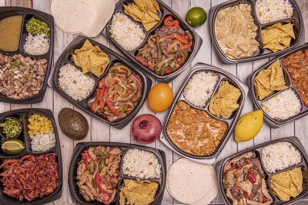 Set of food delivery containers filled with Mexican recipes with stews, nachos, rice, pies, wheat pancakes, whole and sliced citrus