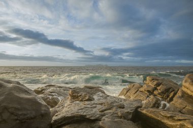 Dalgaların saldırısına uğrayan doğal dalgalar gün batımında ufuktaki bazı adaların görüntüleriyle bulutlarla dolu gökyüzü.