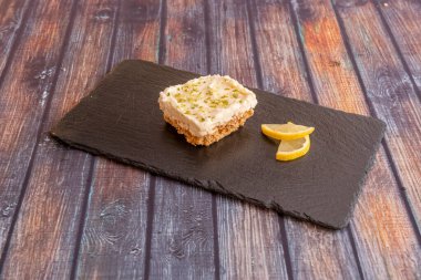 Siyah bir tepside bisküvi tabanlı bir dilim limonlu tart.