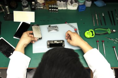 Küçük atölyesindeki akıllı telefonu tamir eden bir operatörü izlemek.