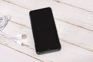 Beyaz kabloyla ahşap bir masaya sıkışmış siyah bir akıllı telefon.