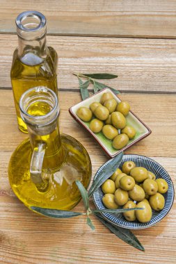 İspanyol zeytinleri, cam şişelerde ekstra saf zeytin yağı ve ahşap bir masada verniklenmemiş zeytin yaprakları.
