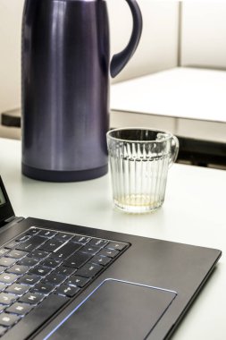 Dizüstü bilgisayar, cam bardak ve termosla birlikte hafif, pürüzsüz bir masaya kurulmuş çay.