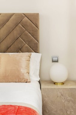 Mermer bir küp, yuvarlak bir lamba ve açık kahverengi kadifeden döşenmiş bir yatak odasının ayrıntıları.
