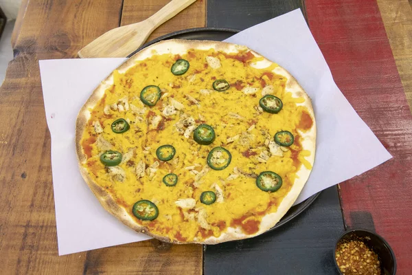 A freshly baked thin crust pizza with chicken, yellow cheese, sliced jalapenos on a parchment paper lined baking sheet