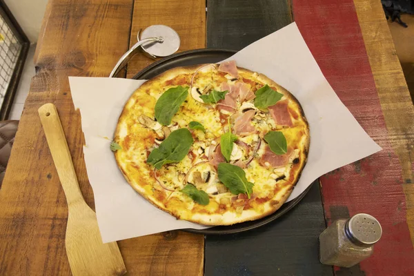 Great Italian thin crust pizza with mushrooms, prosciutto and a lot of basil on wooden table