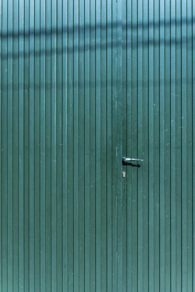 A green metal gate of a detached house with a handle and lock