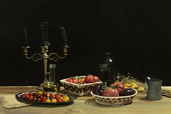 Still life with various types of delicious ripe tomatoes, cherry tomatoes, glass oil can, dried flowers and a candlestick with black candles