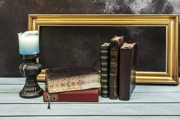 A still life picture with old books, a candle and a golden frame