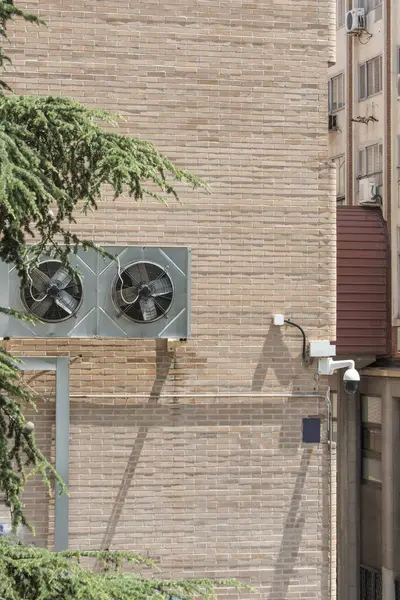 Surveillance camera and air conditioning fans on a wall of a clay brick building