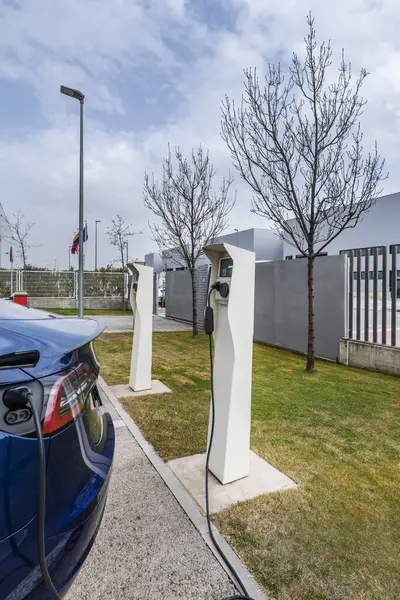 Several fast charging stations for electric vehicles in an open-air car park next to the garden
