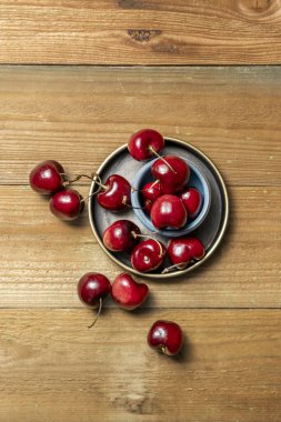 Küçük yuvarlak kaseler ve verniklenmemiş ahşap arka planda lezzetli olgun kirazlar.