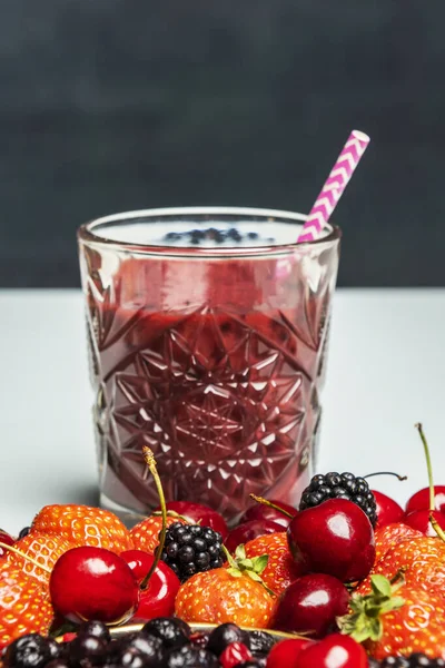 Glass with freshly squeezed berry juice with red cherries, ripe blackberries and fresh strawberries
