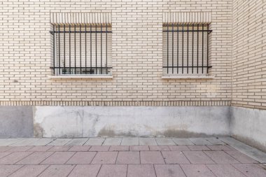Metal parmaklıklı ve beyaz tuğlalı iki pencereli bir binanın duvarı.