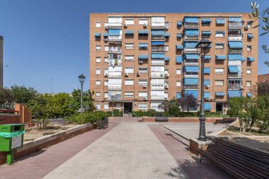 Ahşap bankları ve bitkileri olan dinlenme ve dinlenme alanı olan bir konut binasının ön cephesi.