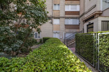 Çitler, metal çitler, kaldırım taşı zeminleri ve ortak alanlarda onlara erişimi olan küçük ağaçlı bahçeler arasında bir yürüyüş.