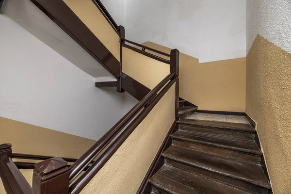 Old stairs with brown wooden railings and stairs and dark cream and white gotelet walls