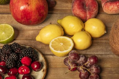 Olgun kirazlar, çekirdeksiz üzümler, limonlar, limonlar ve böğürtlenler verniksiz ahşap bir masada.