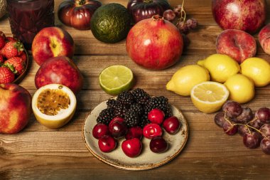 Olgun kirazlar, çekirdeksiz üzümler, limonlar, limonlar ve verniksiz ahşap bir masada böğürtlenlerle dolu sakin bir hayat.