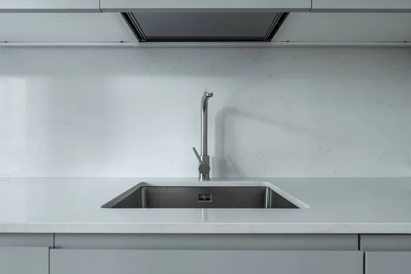 stainless steel kitchen sink embedded in a polished white stone countertop to match the wall materiall