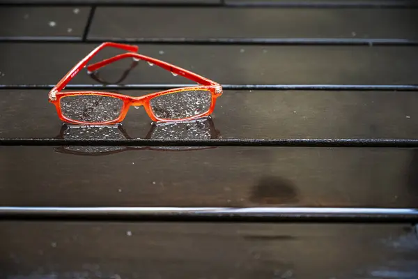 Orange rimmed reading glasses wet with raindrops on a wet wooden plank floor