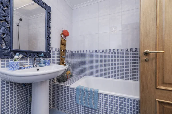 A bathroom with blue and white tiles, a dividing border, a white bathtub,
