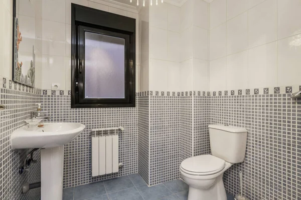 A bathroom with stoneware and white tiles, a dividing border, porcelain sink, matching toilet