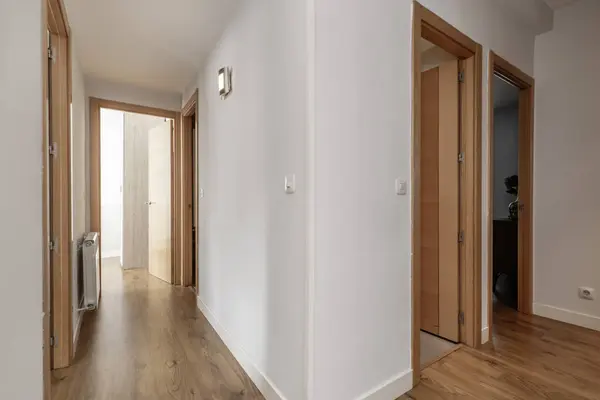 Hallway in a house with light wood floors and French oak doors to other rooms and plain white walls