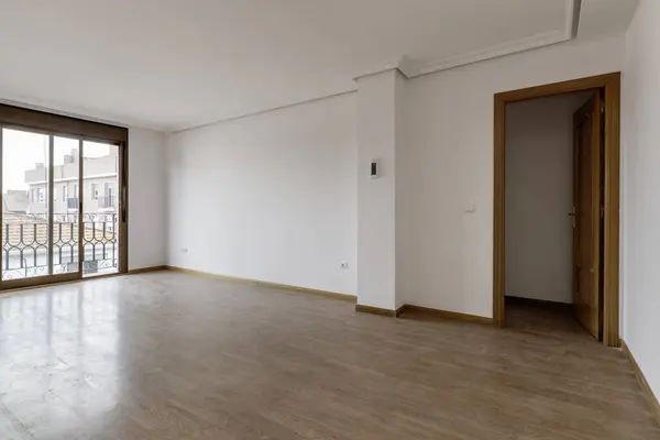 Empty living room with dusty wooden floors and a French window